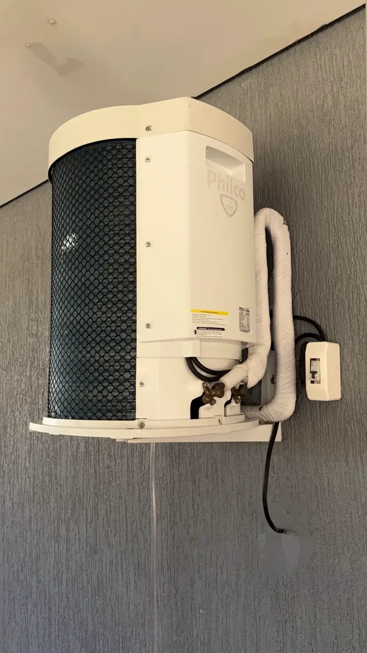 Condensadora Philco fixada em suporte numa parede cinza, com a tubulação isolada e a tomada ao lado.