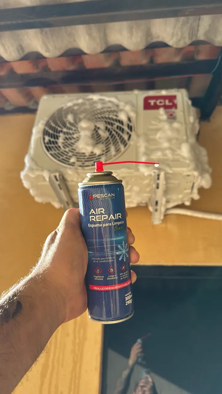 Mão segurando um spray de limpeza diante de uma condensadora TCL.
