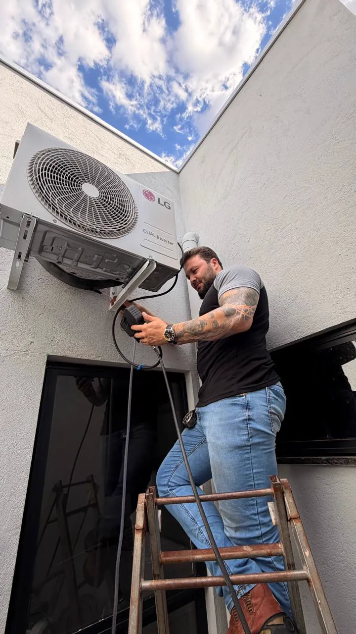 Mateus Henrique, dono da MH Clima Ar, em cima de uma escada fazendo a ligação de uma condensadora LG na parede.