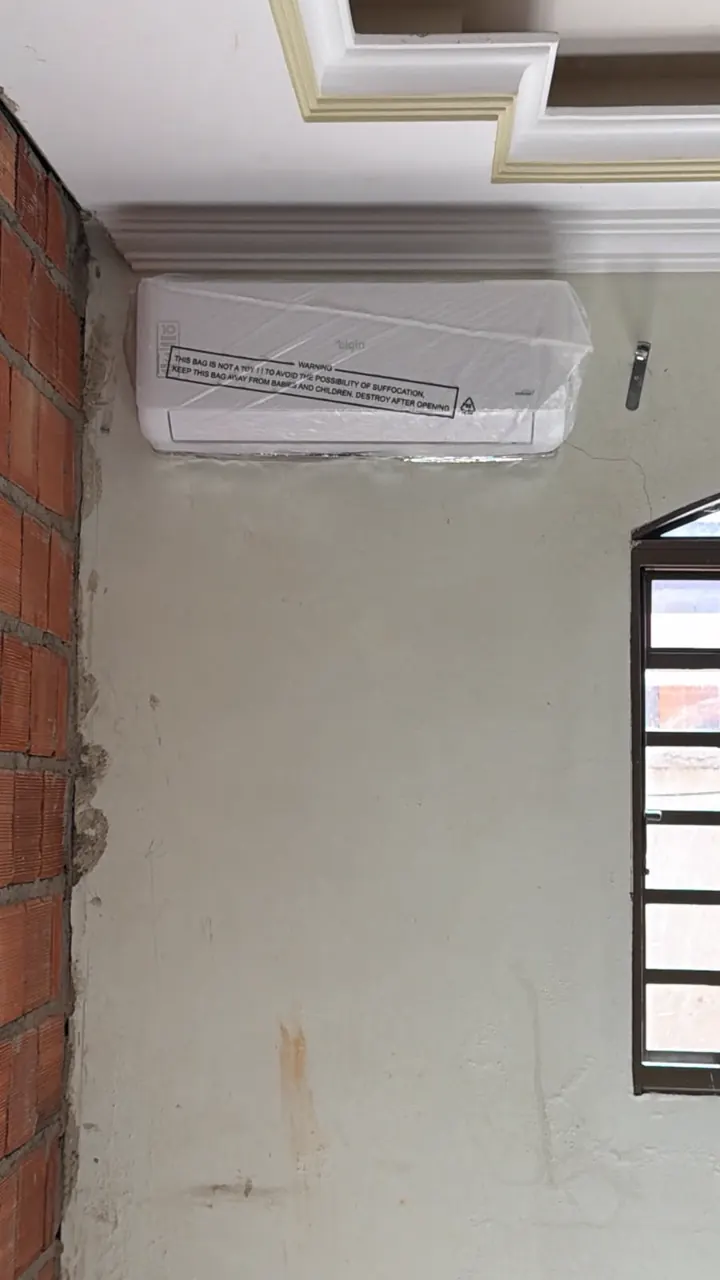 Split novo, ainda no plástico, instalado numa parede em obra, com o tijolo aparente ao lado e a tubulação embutida.