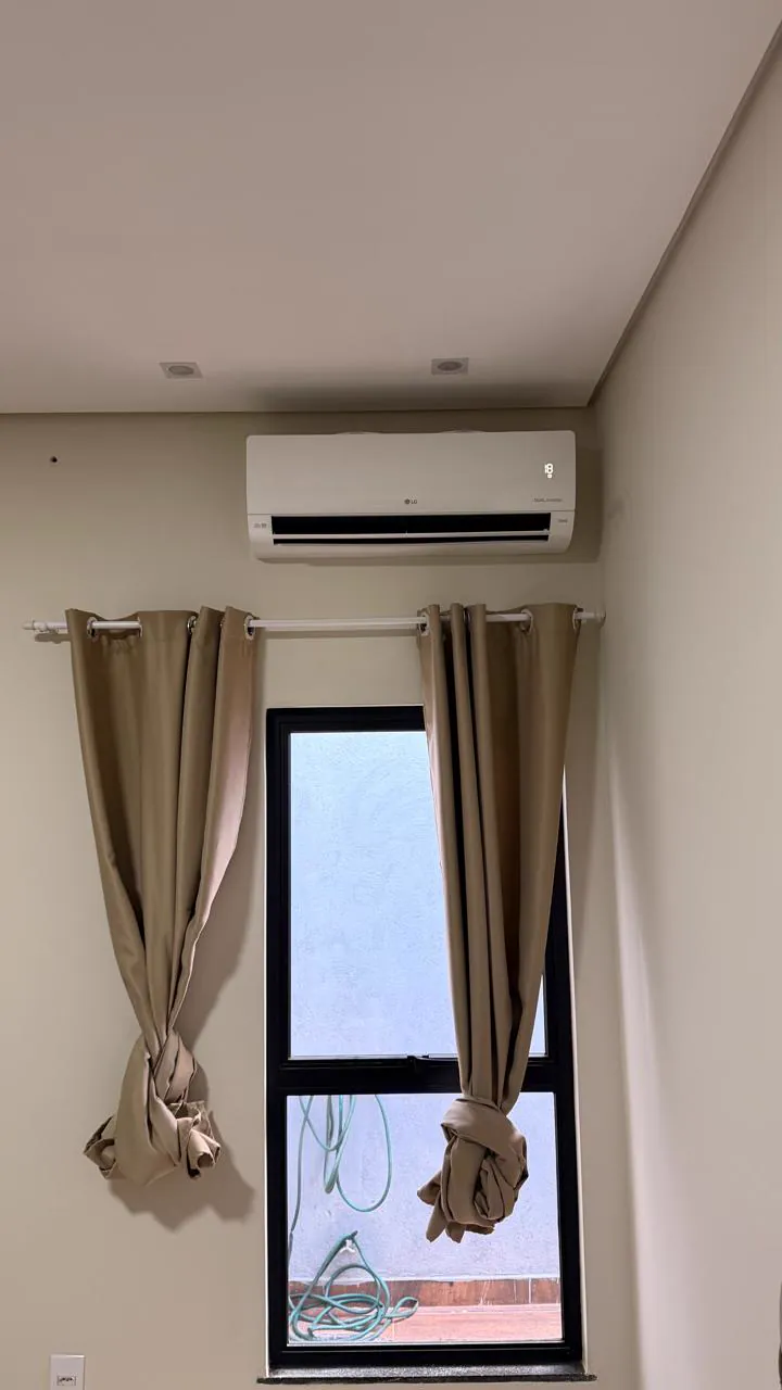Split LG instalado no alto da parede de um quarto, acima da janela com cortinas.