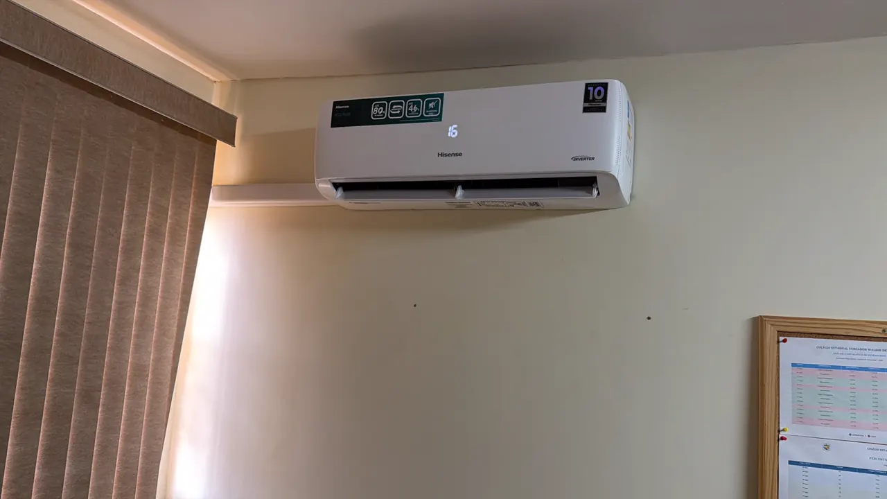 Split instalado no alto da parede de uma sala, ao lado de uma persiana vertical.